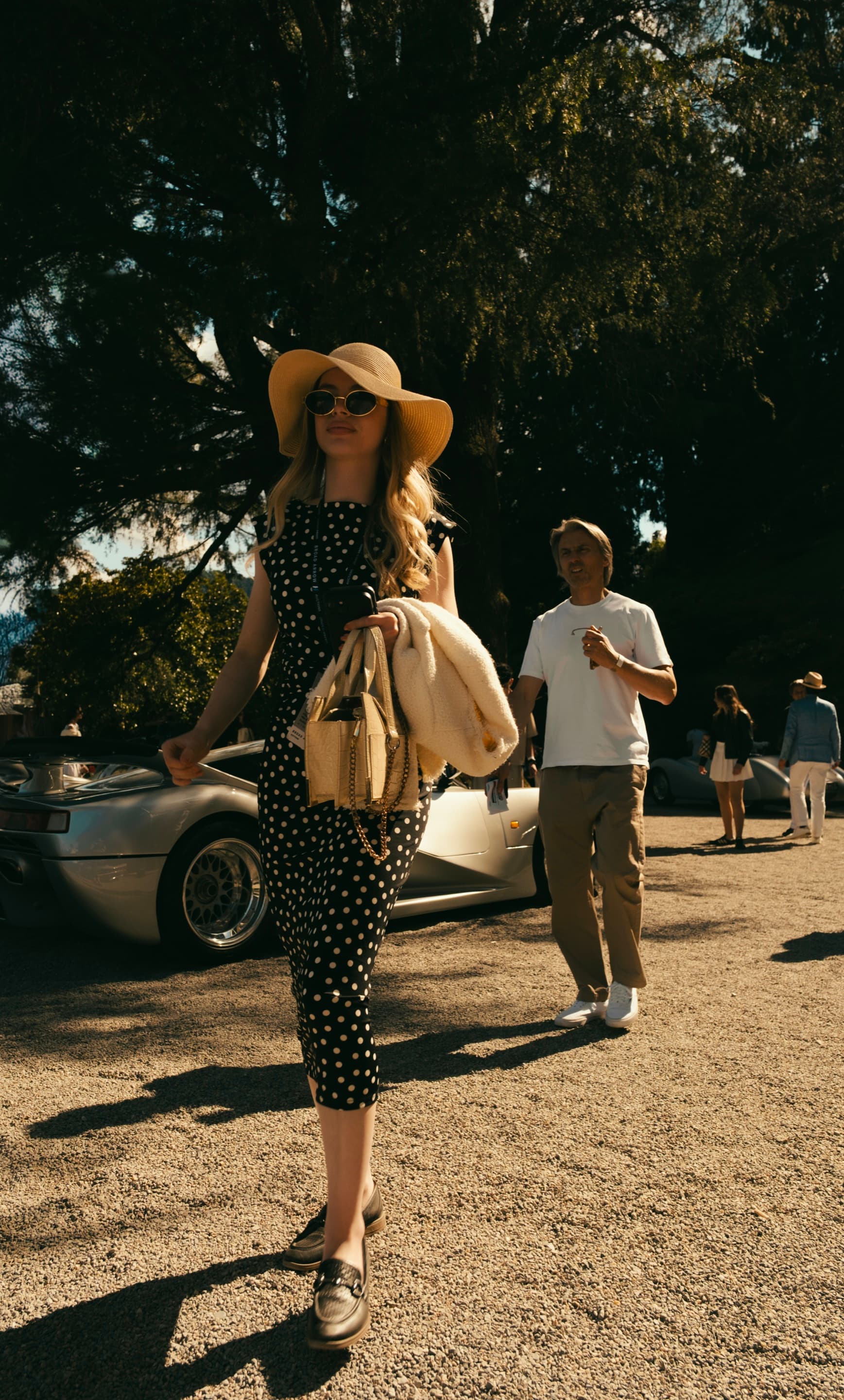 A guest in polka-dot couture walking past a vintage Mercedes