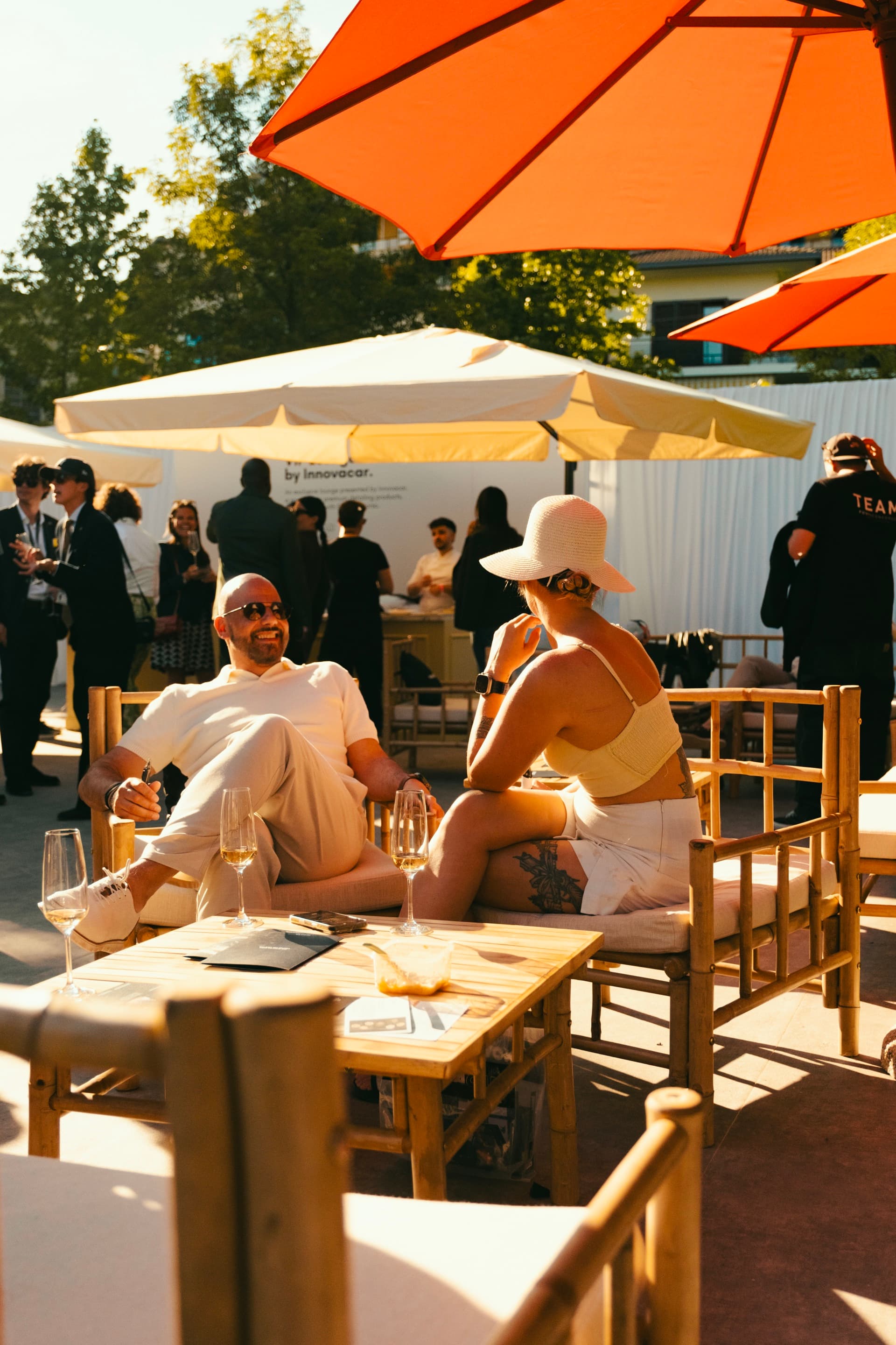 Bamboo chairs, orange umbrella, two guests in the gardens at golden hour